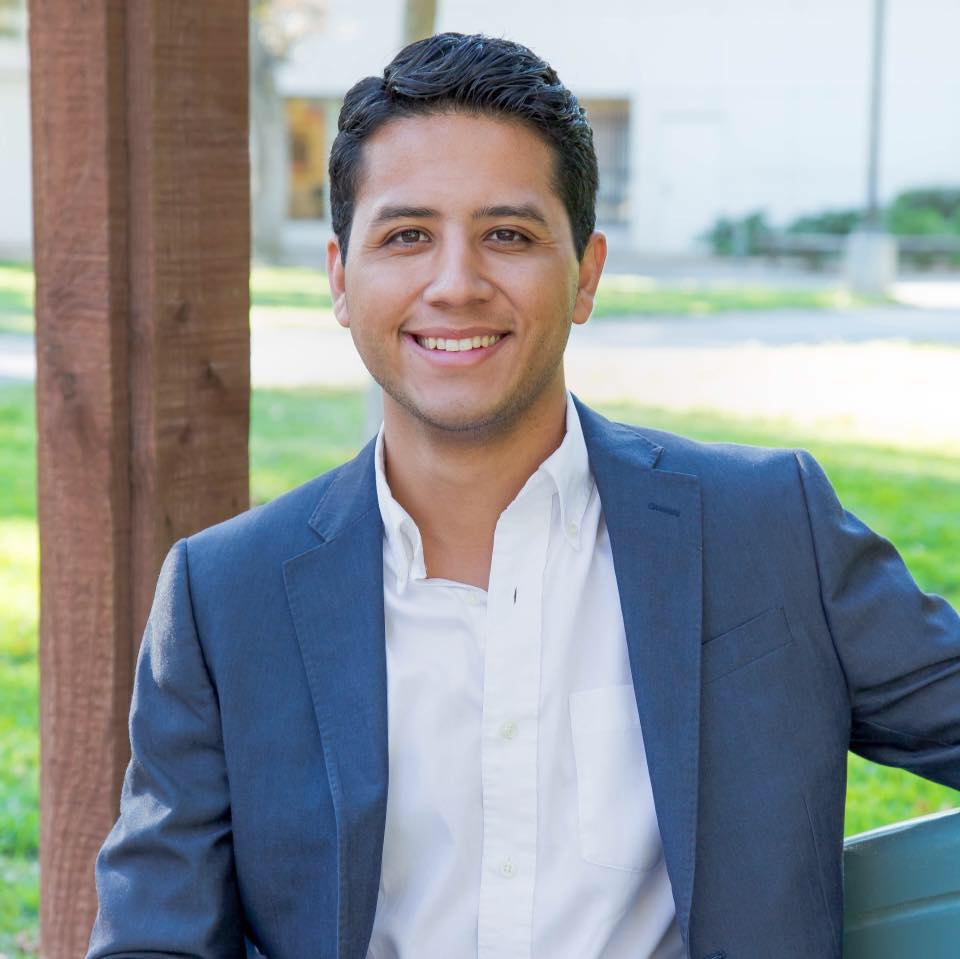 Headshot of Andres P Chavez smiling and wearing a blue blazer over an open-collared white shirt.