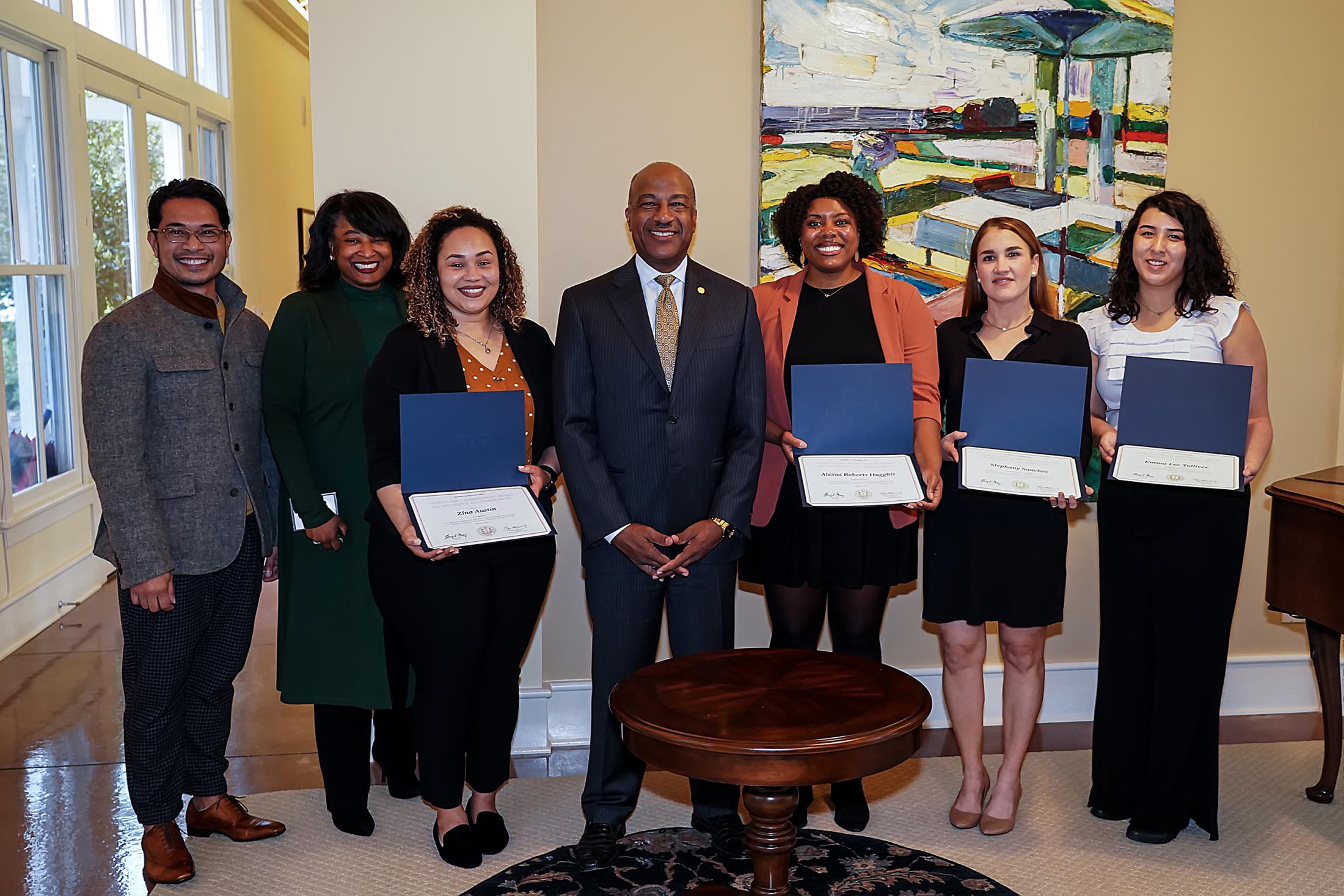 Group of people holding awards while standing in front of a painting with Chancellor Gary May in the center of the group.