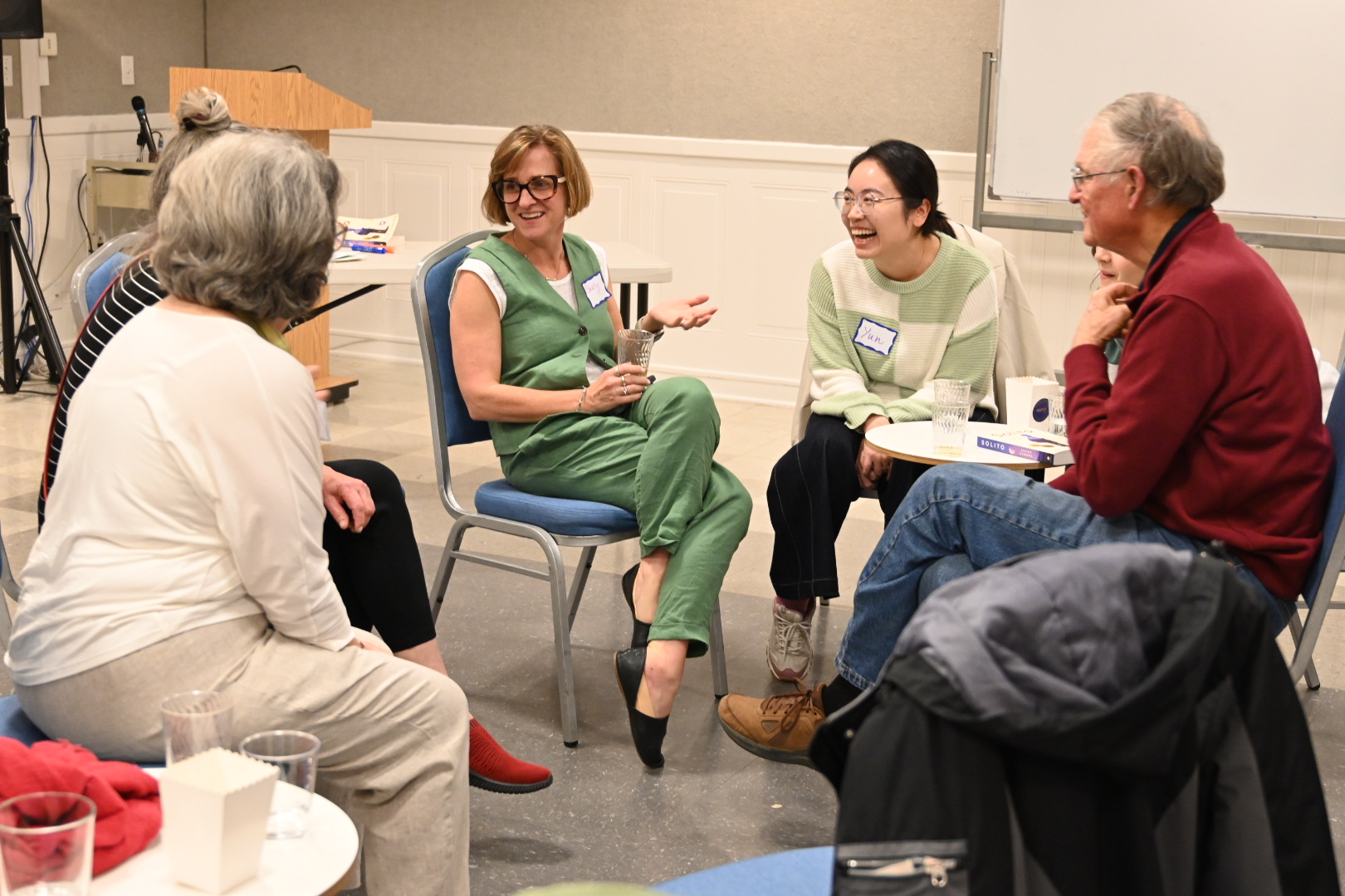 Woman in green pant suit sits in the center of a seated group of book club members engaged in conversation at the International House Davis.