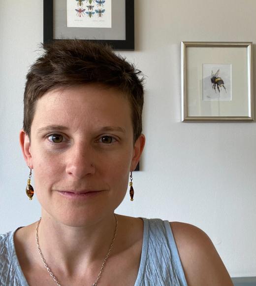 Woman with short hair is in a room with a framed picture of a bee behind her.