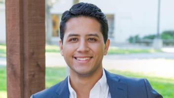 Headshot of Andres P Chavez smiling and wearing a blue blazer over an open-collared white shirt.