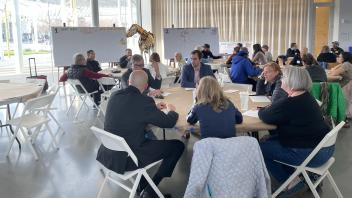 Groups of people sitting at round tables and in conversation with someone speaking near a white board
