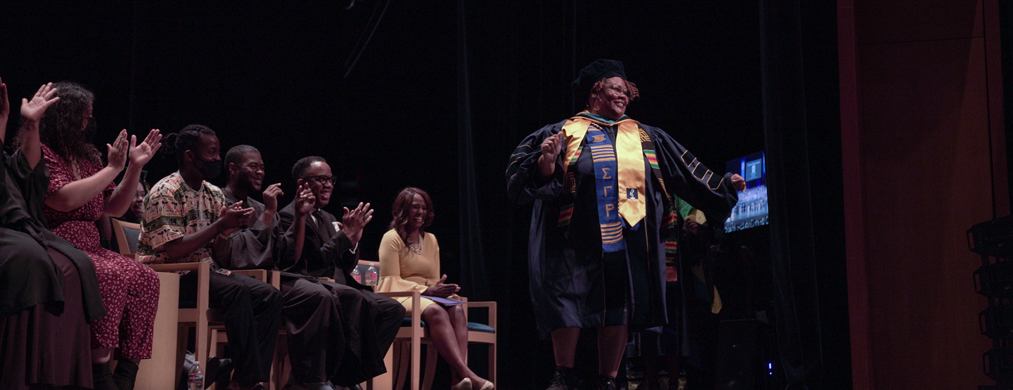 Grad student walking across the stage and people clapping.