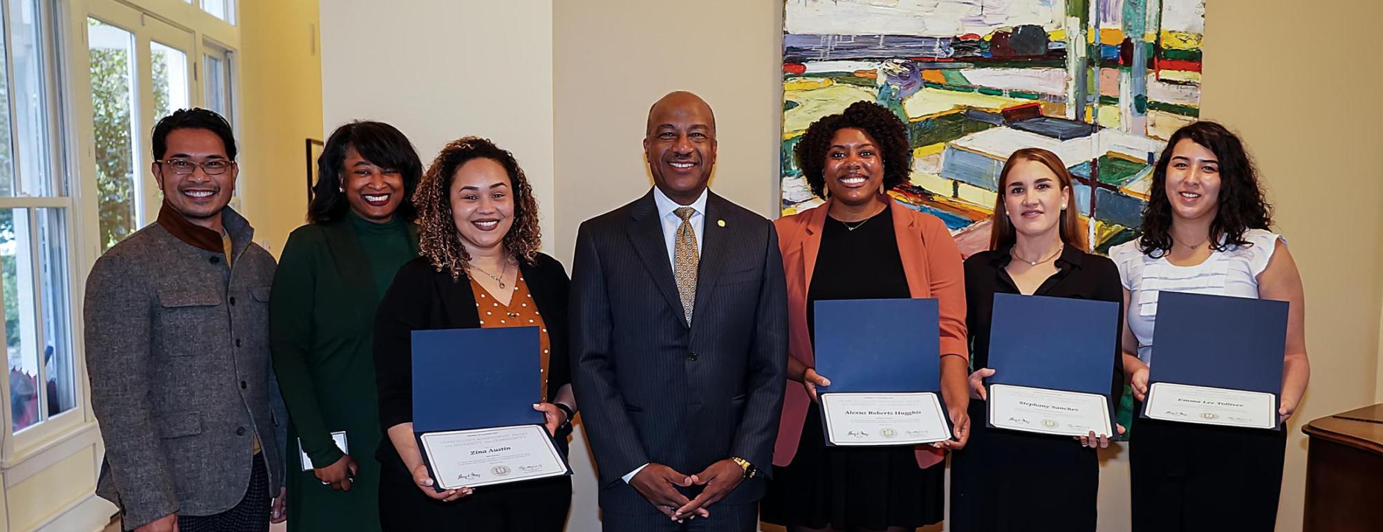 Group of people holding awards while standing in front of a painting with Chancellor Gary May in the center of the group.