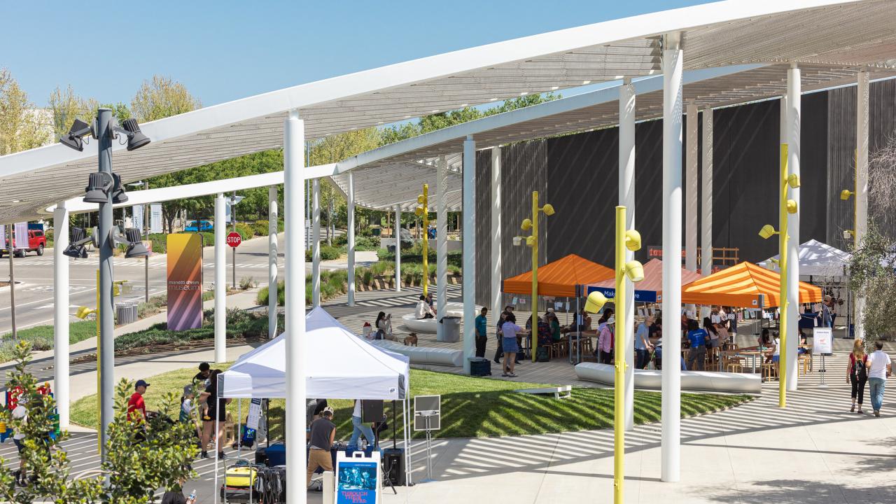 Outdoor event with orange and white tents at the Manetti Shrem Museum Plaza on a sunny day.