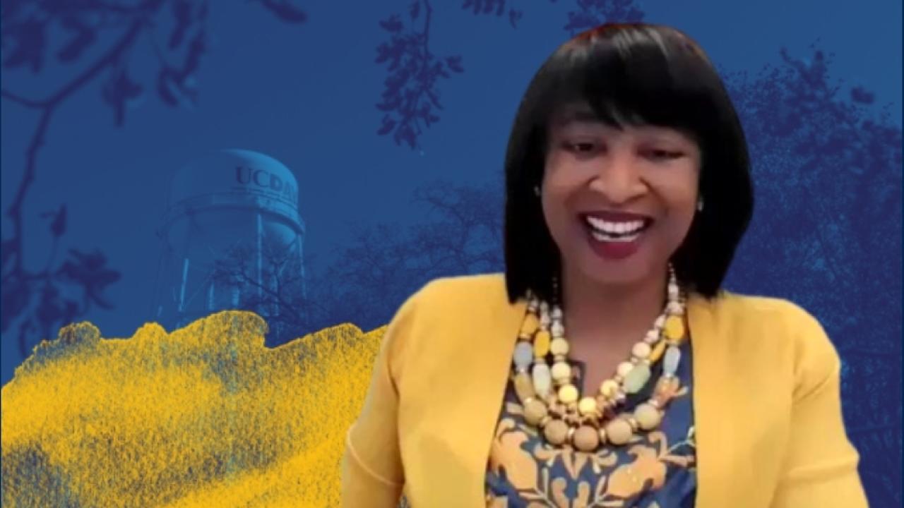 A woman in a yellow jacket in front of a screen with blue and yellow watercolors. 