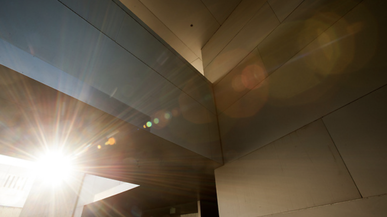 Sunlight shining through the angular walls of a modern building, creating lens flares and rays of light across the geometric surfaces.