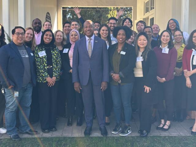 A group of UC Davis faculty and staff pose for a photo with Chancellor Gary S. May during the 2025 AAC/ERG Breakfast. The group stands smiling outdoors in front of a white building with columns, wearing name tags and business or business-casual attire. 