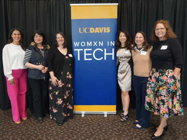six women stand with Womxn in Tech banner