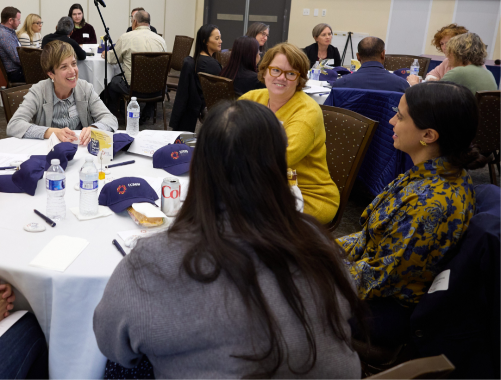 People participating in a discussion around a table with items like water bottles and Blue UC Davis caps.