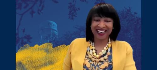 A woman in a yellow jacket in front of a screen with blue and yellow watercolors. 