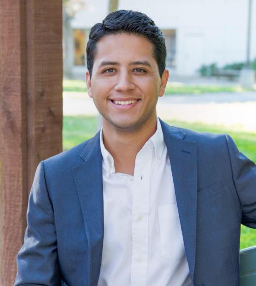 Headshot of Andres P Chavez smiling and wearing a blue blazer over an open-collared white shirt.