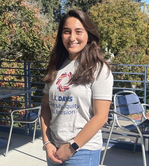 Marisa Davidson stands on patio in sunshine, wearing tshirt with UC Davis DEI logo on it.