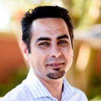 Joshua Hori headshot wearing a striped shirt in front of a blurred exterior background.