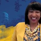 A woman in a yellow jacket in front of a screen with blue and yellow watercolors. 