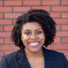 Portrait of a woman of color with shoulder-length dark curly hair wearing a black top..