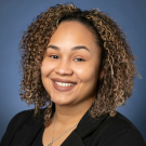Portrait of a woman of color with shoulder-length curly hair wearing a black top.