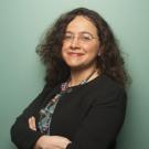 headshot of Mariel Vázquez standing against a green wall with arms folded across her chest