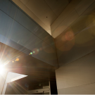 Sunlight shining through the angular walls of a modern building, creating lens flares and rays of light across the geometric surfaces.
