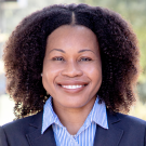 Smiling professional headshot of woman with curly hair, blazer and striped collared shirt