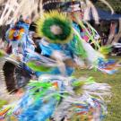 A dancer in vibrant traditional attire performs on grassy grounds at a cultural festival.